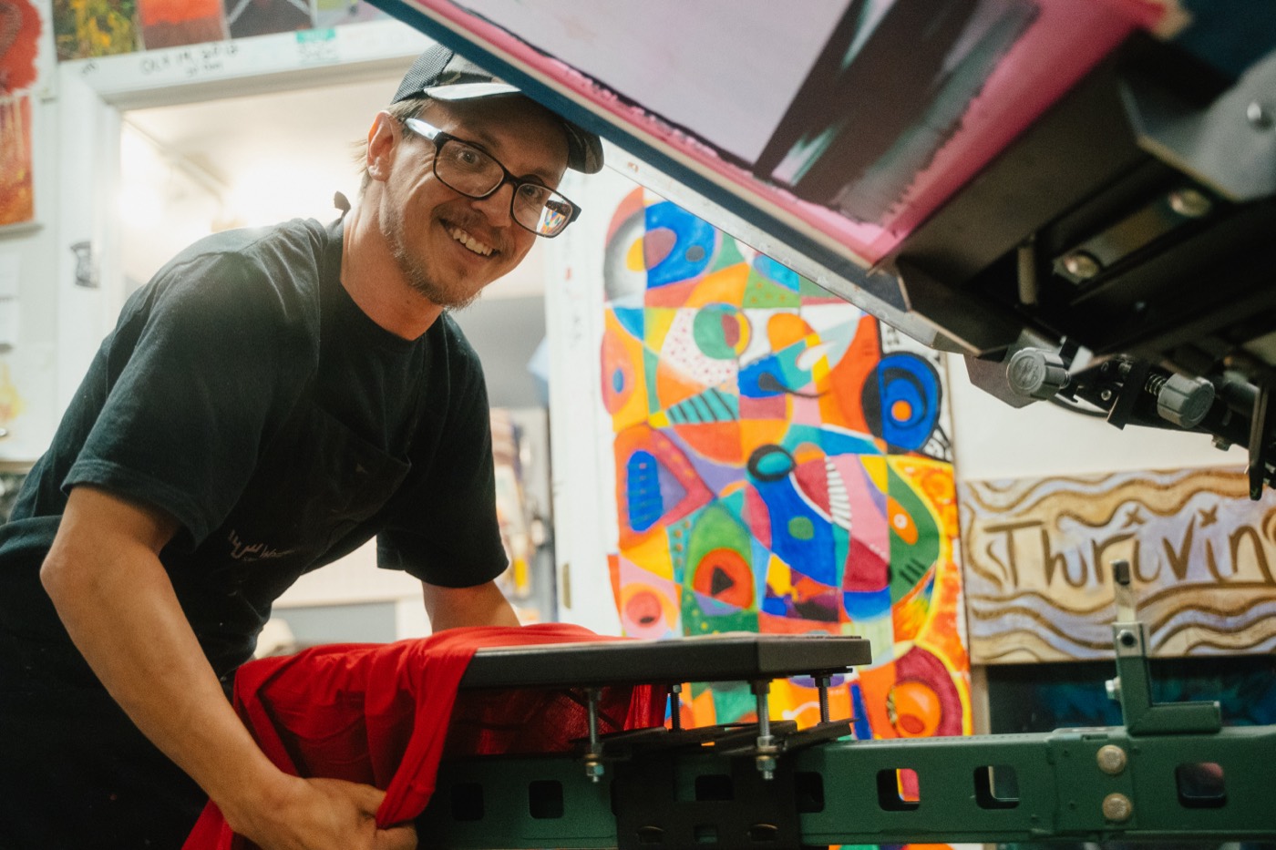 A smiling crew member at the press beside a freshly printed shirt
