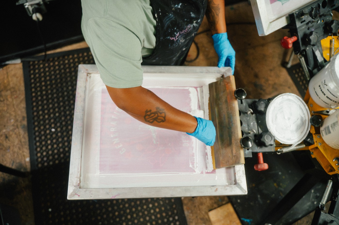 Hands pulling a squeegee across a screen on the press